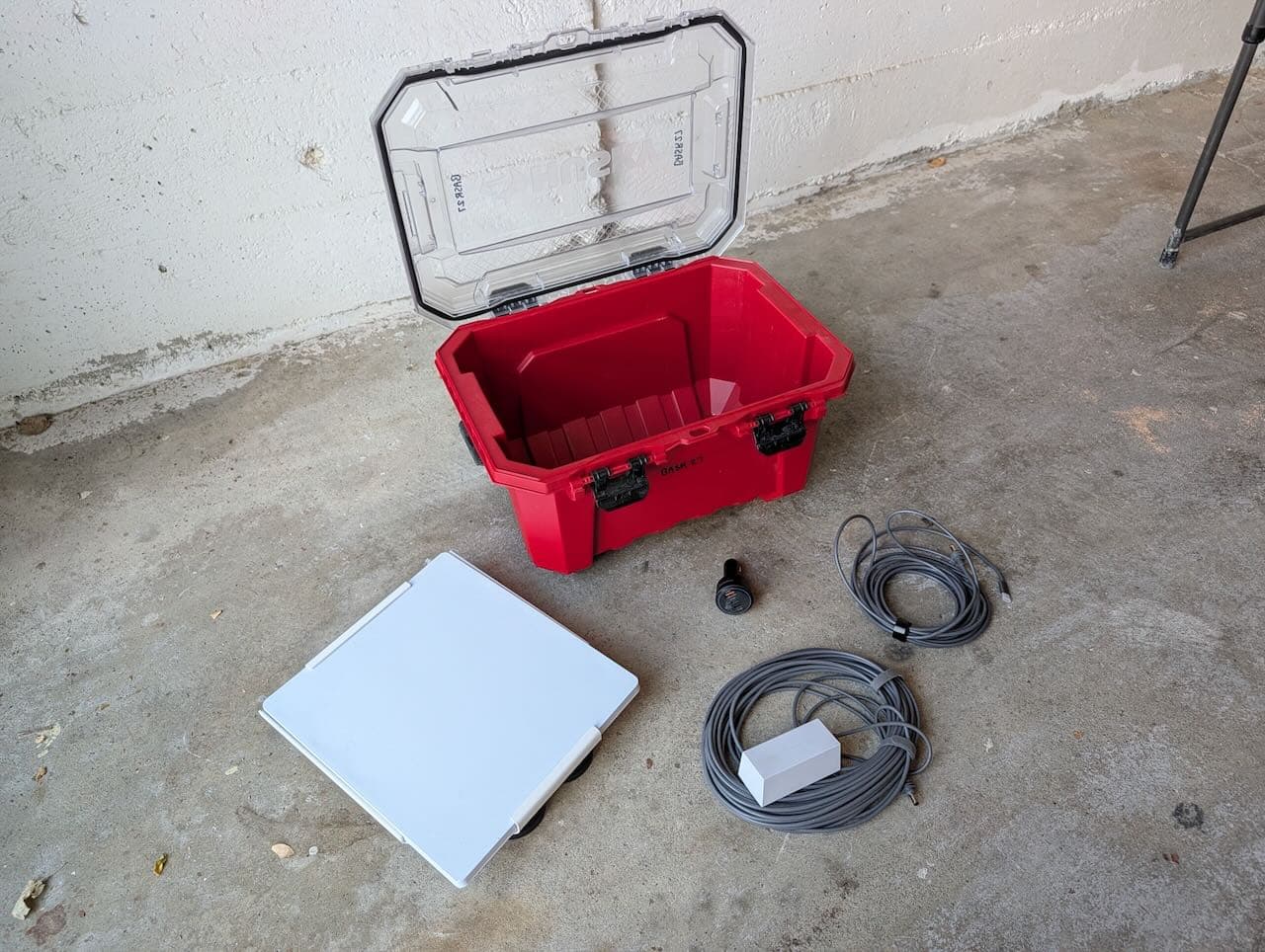 The complete Starlink rental kit showing the red waterproof carrying case, white mounting bracket with magnets, Starlink Mini dish, power cables, and cigarette lighter adapter on concrete.